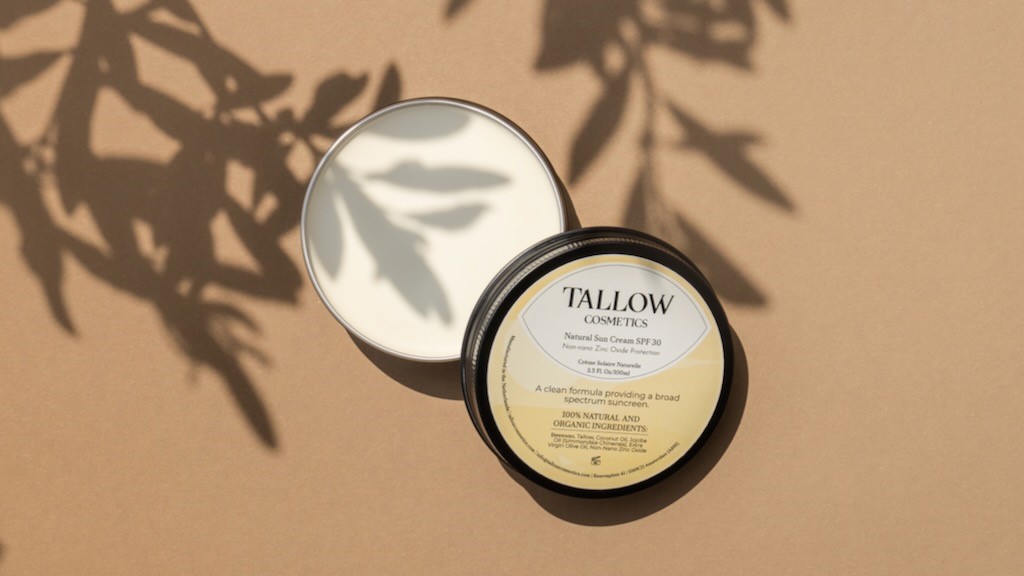 Minerální opalovací krém Tallow Cosmetics s pečujícími oleji a hovězím lojem v hliníkové dóze na pláži.